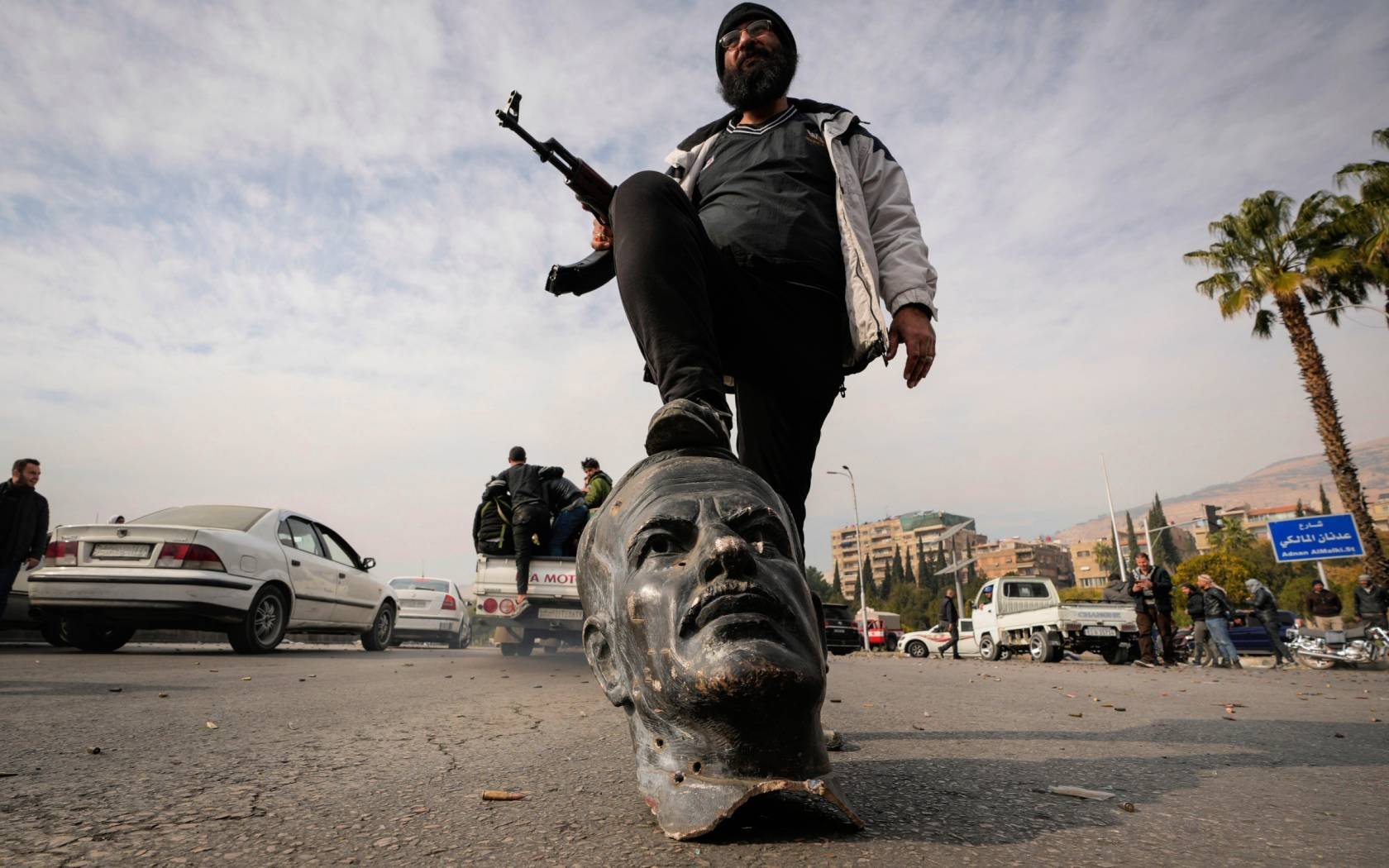 An opposition fighter steps on a broken bust of the late Syrian President Hafez Assad in Damascus, 8 December 2024.