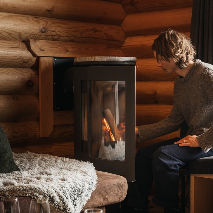 man l&auml;gger in ett vedtr&auml; i kaminen p&aring; Solhyllan i K&aring;ppas stugby