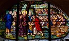 A stained glass of Jesus multiplying loaves and fish.