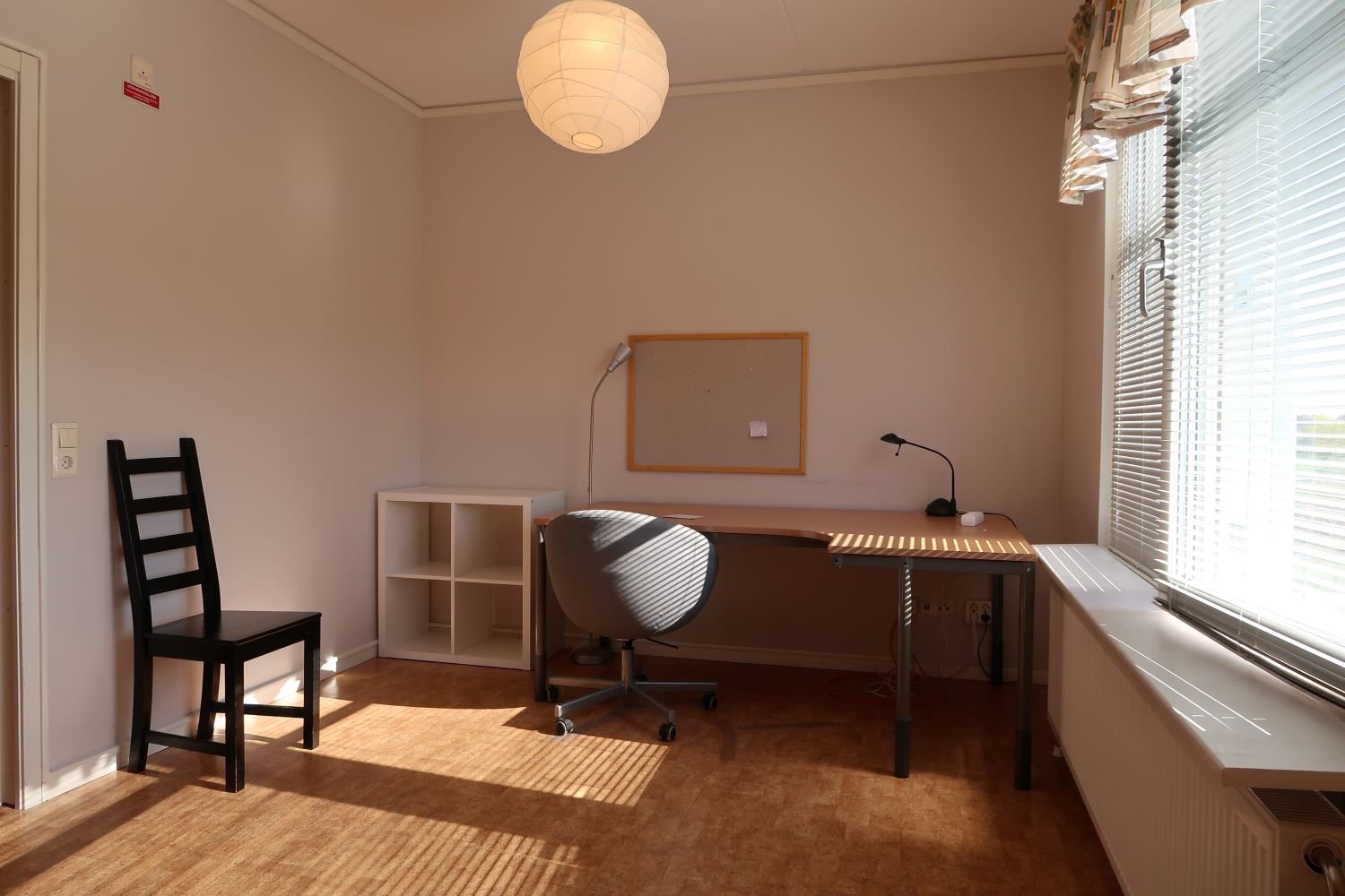 Studentroom with desk, deskchair, storage unit and notice board.