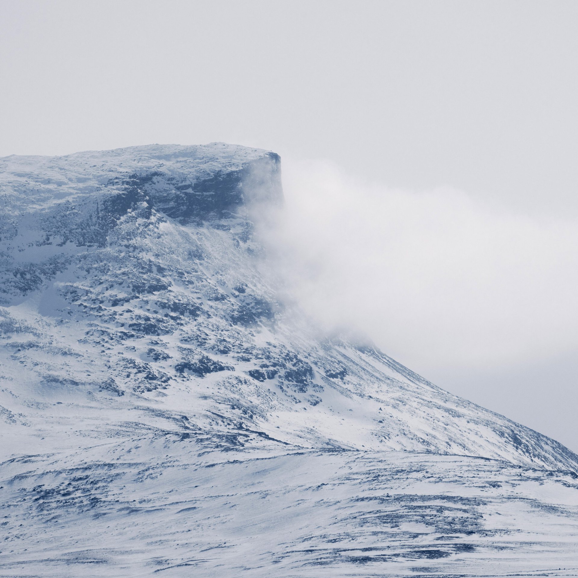 en sn&ouml;bekl&auml;dd fj&auml;lltopp omgiven av moln