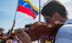 A violinist plays in front of a Venezuelan flag.