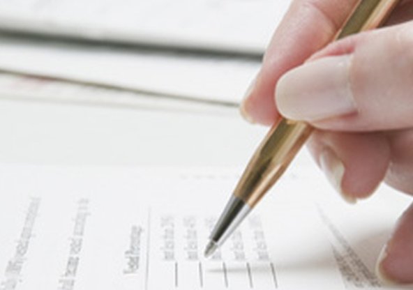 En hand håller i en guldpenna och fyller i blankett