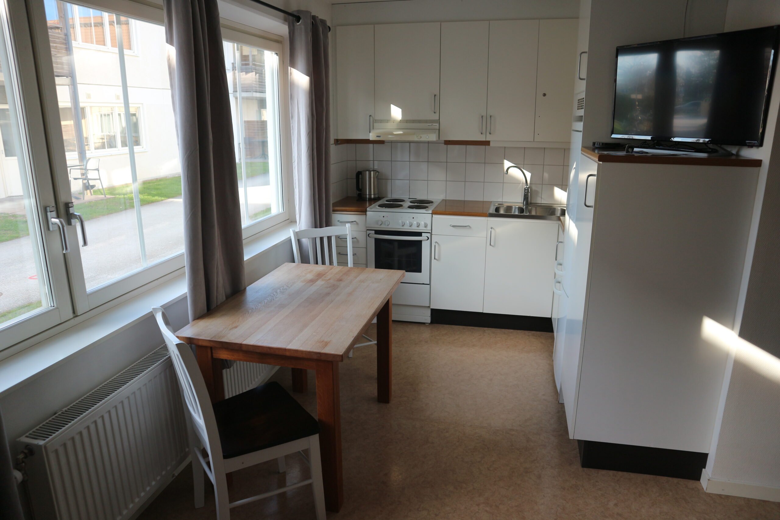 Student room kitchen with stove, oven, cupboards, sink, refrigerator, freezer, tv, kettle, table and chairs.