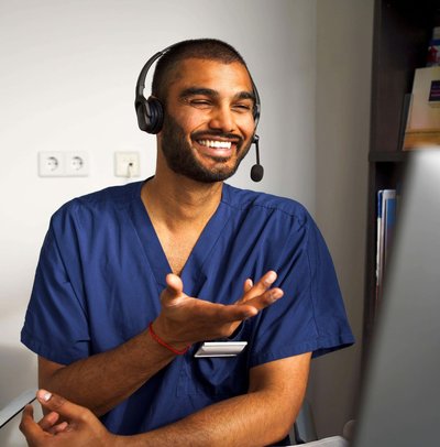 Happy male medical professional wearing headset assisting patient through video call in clinic at hospital