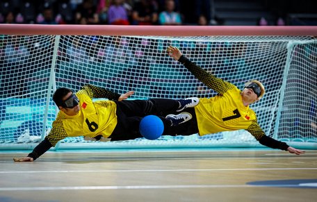 Två målvakter i goalball slänger sig åt varsitt håll och räddar bollen.