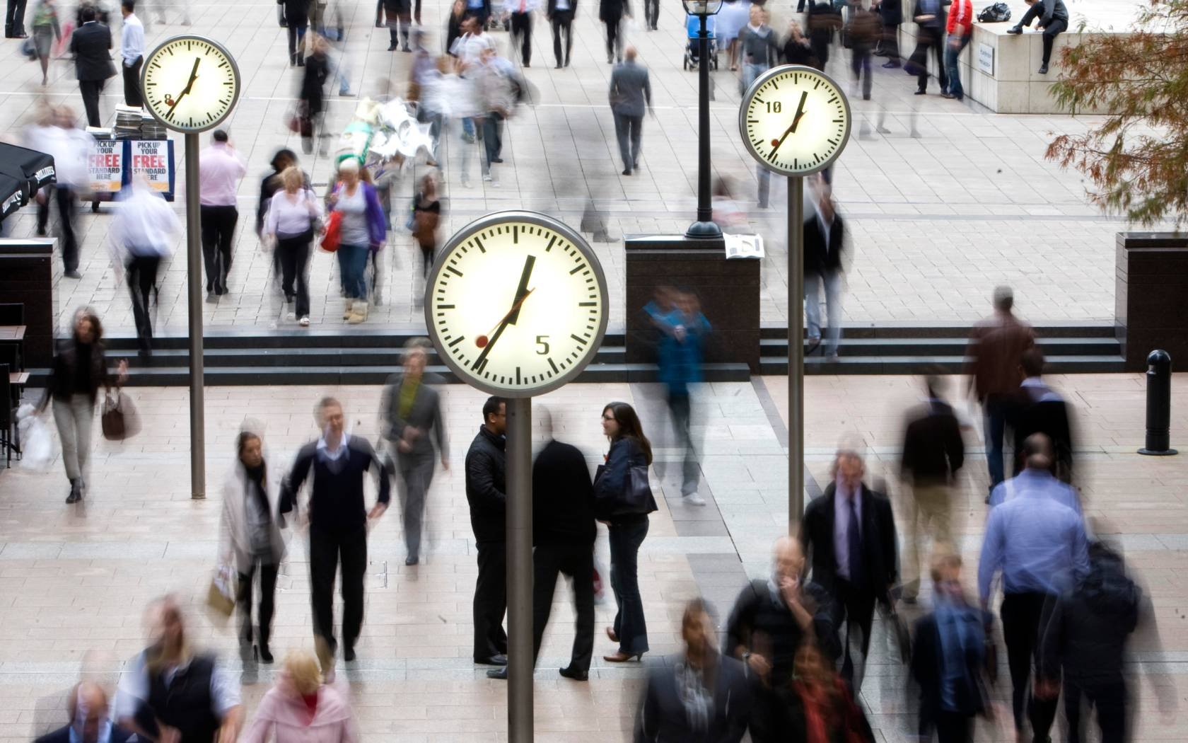 Pedestrians walk past clocks in the financial district of Canary Wharf, London