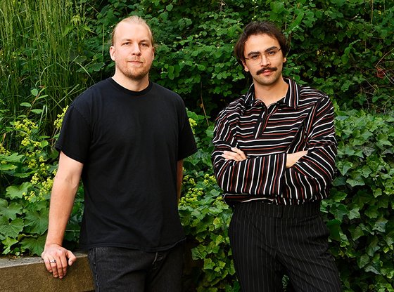 Afrang Nordlöf Malekian (höger) och Roger Smeby (vänster) står sida vid sida framför en mur med grönskande löv i bakgrunden, båda har fokuserade uttryck och blicken i kameran.