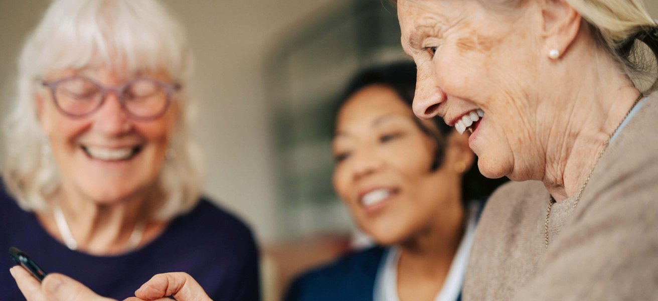 Happy senior woman using smart phone while spending leisure time in retirement home