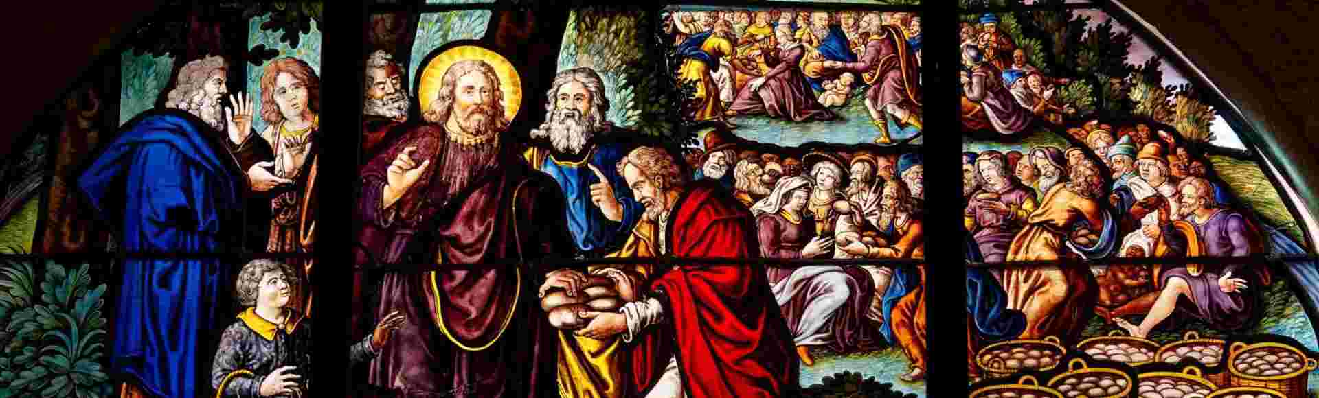 A stained glass of Jesus multiplying loaves and fish.