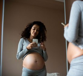 Reflection of pregnant woman taking selfie on smart phone at home