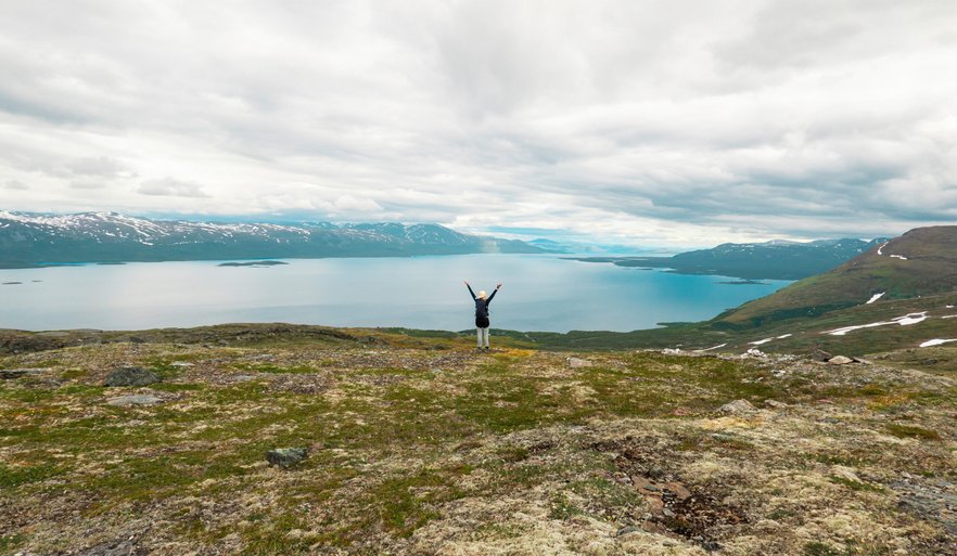 kvinna med armarna upp&aring;tstr&auml;ckta p&aring; fj&auml;llet med Tornetr&auml;sk som utsikt