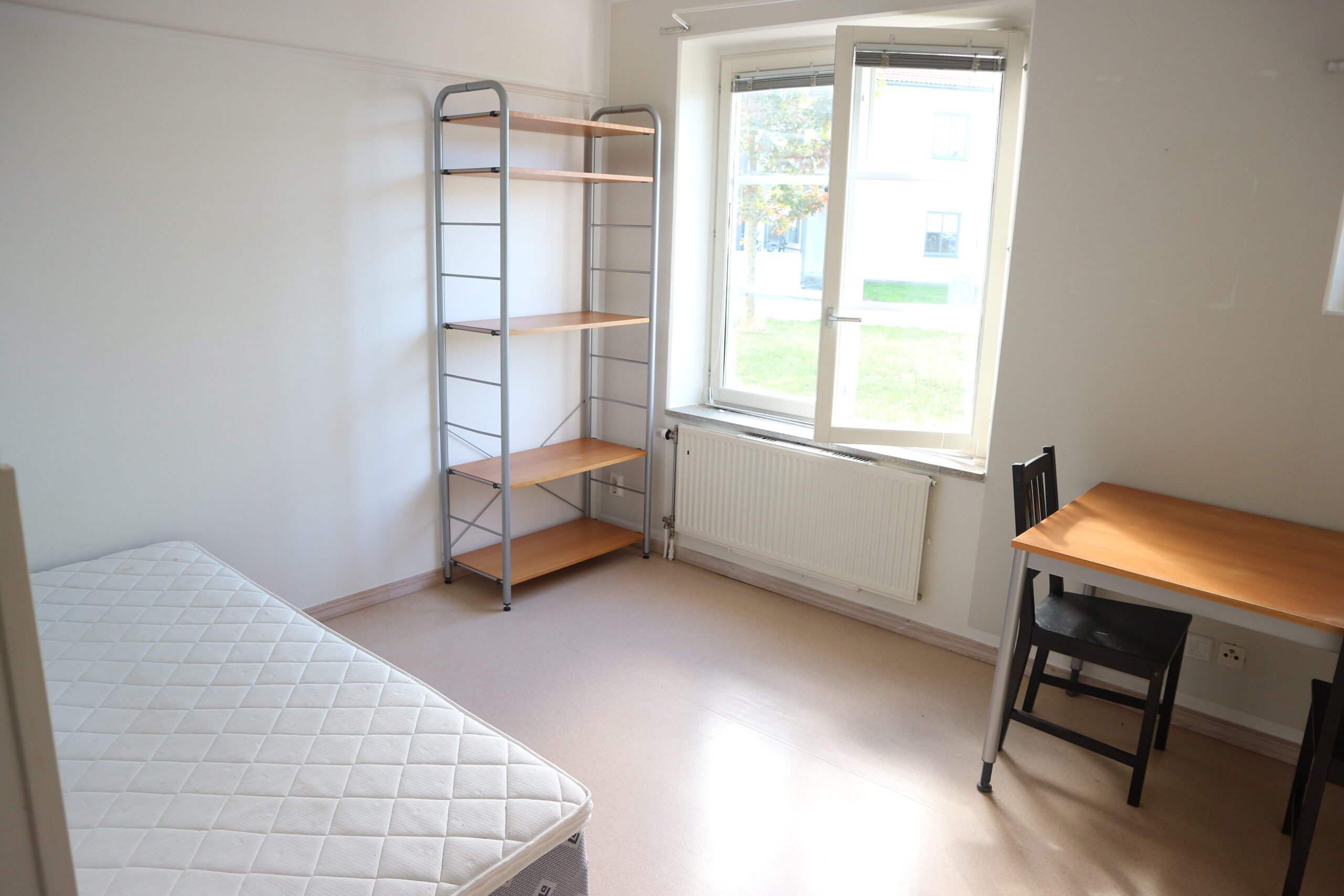 Student room with bed, bookshelf, table and chair.