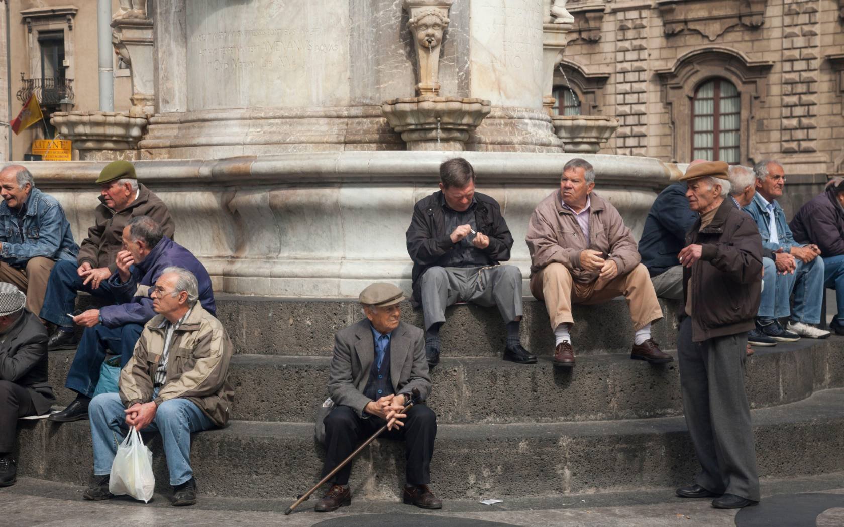 Aged men gathering at Fontana dell' Elefante in Piazza Duomo, Catania, Sicily.