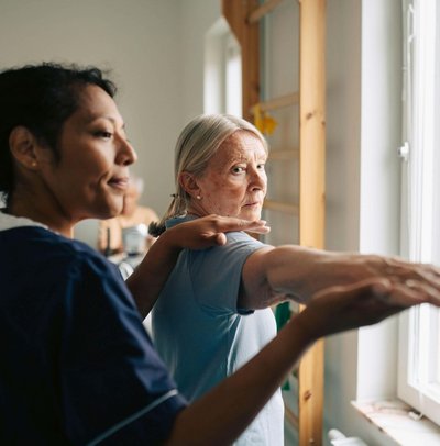 Female therapist helping senior woman with stretching exercise at rehabilitation center