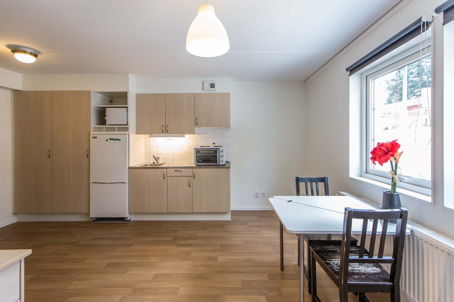 Studentroom with kitchenette, refrigerator, freezer, sink, oven, stove top, table and chairs.