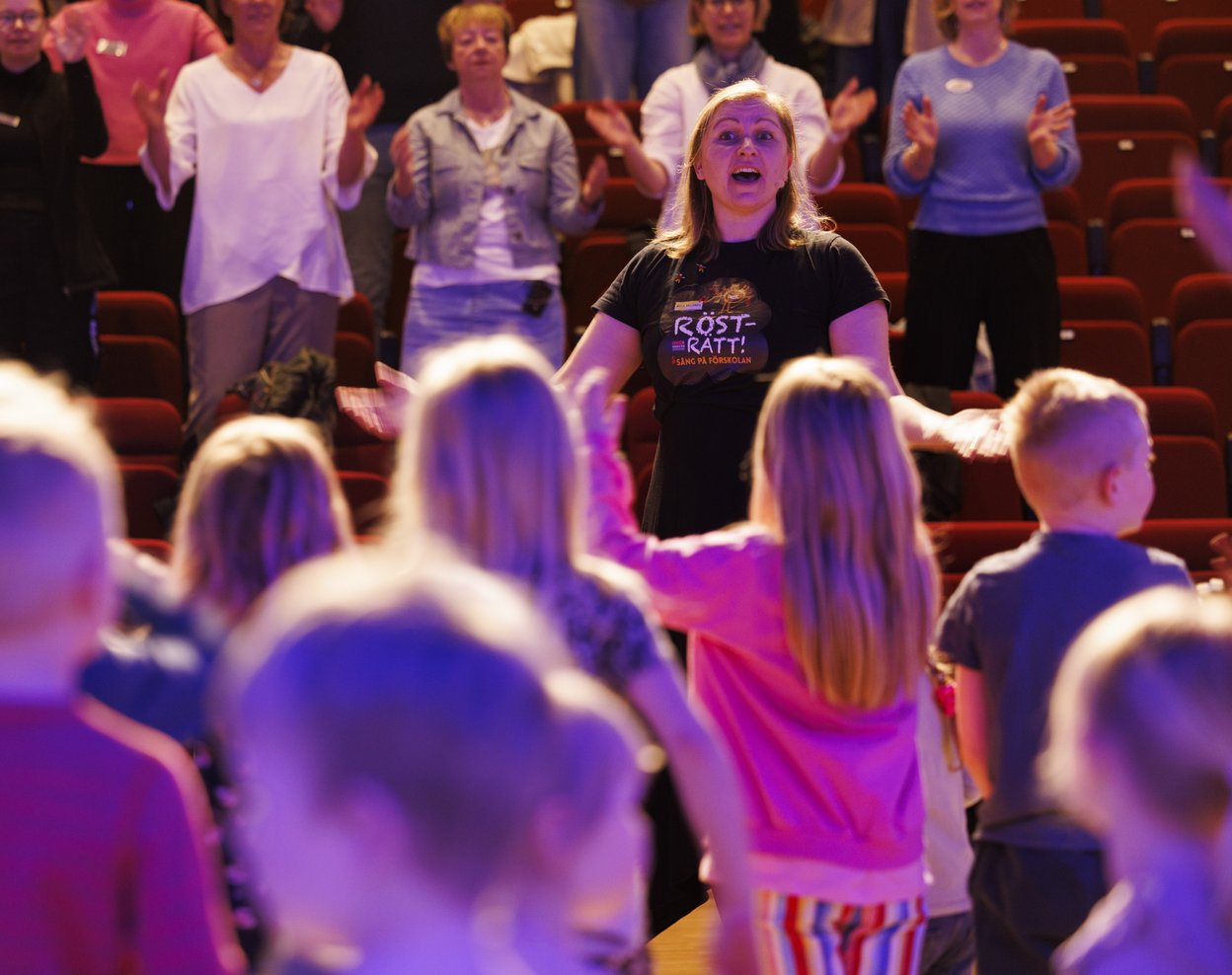 Sånglärare som glatt sjunger med en grupp barn i förskoleåldern.