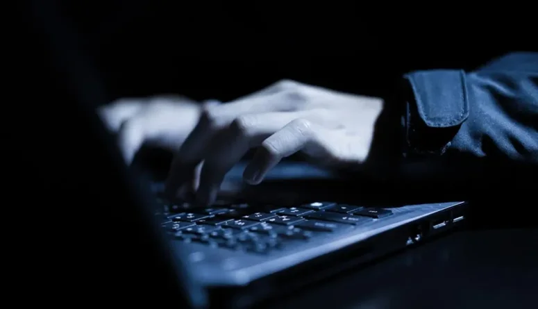 Tumma lähikuva henkilöstä, joka kirjoittaa kannettavalla tietokoneella.