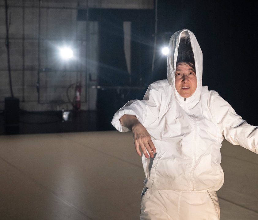 En person i vit luvjacka, shorts och höga strumpor, luvan står upp högt ovanför huvudet.