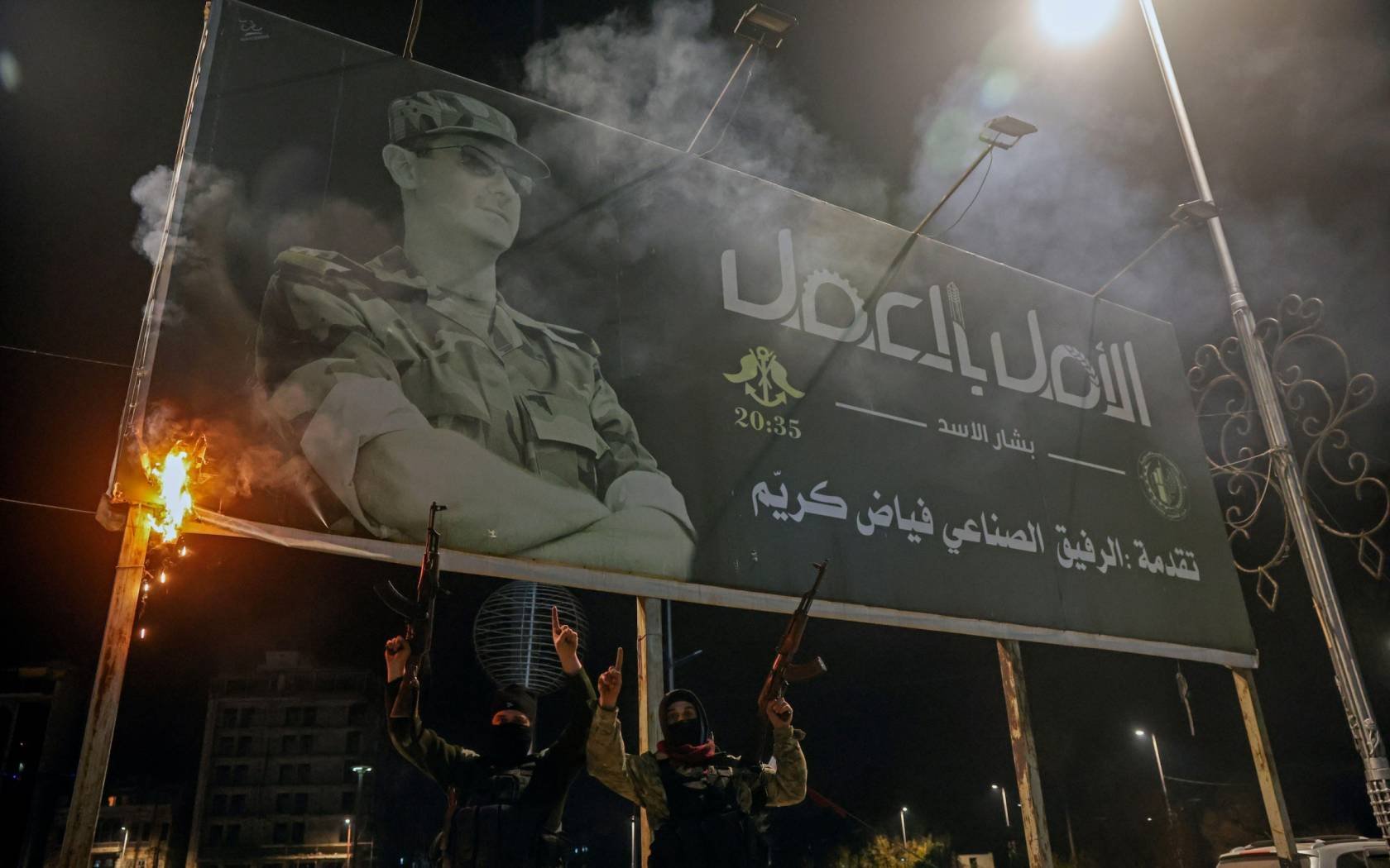 Opposition fighters hold up their guns as they pose for photos under a billboard depicting Syrian President Bashar Asad in Aleppo, Syria.