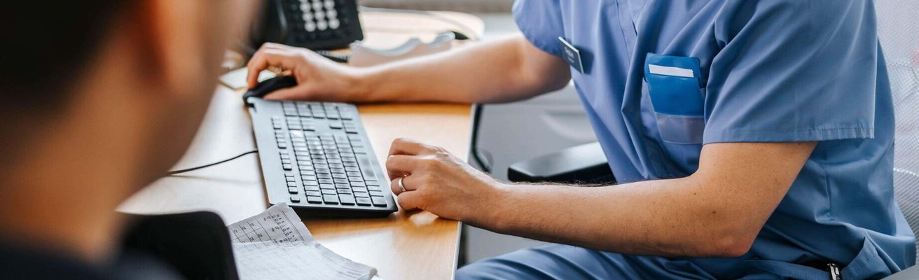 Focused male medical expert checking medical record of patient on computer while sitting on chair in examination room