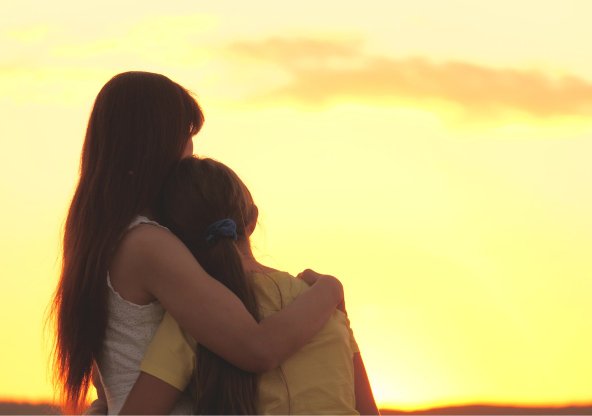 Ryggtavla av kvinna som håller om flicka och tittar ut över solnedgång