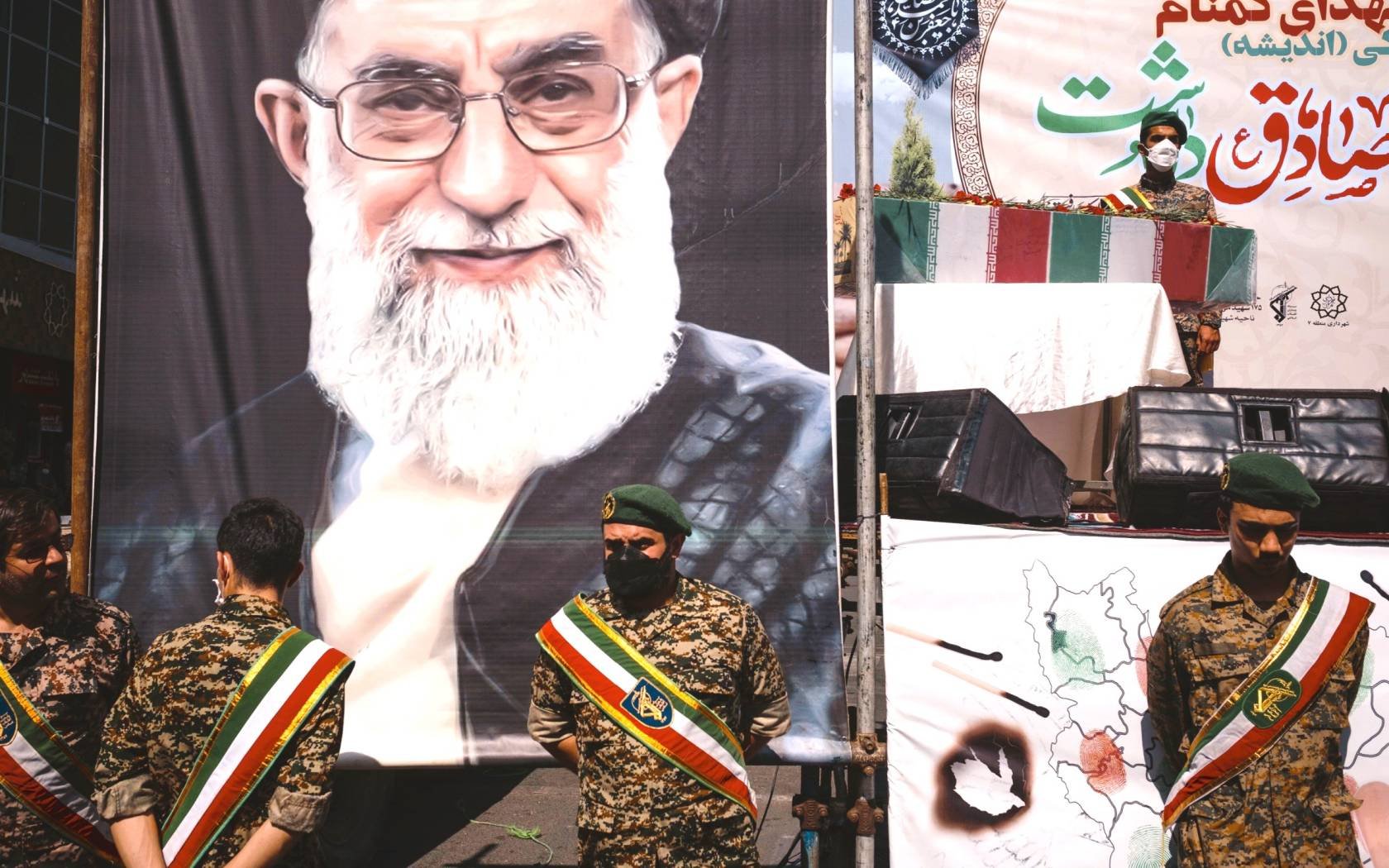 Members of the Islamic Revolutionary Guard Corps (IRGC) stand next to a poster of Ayatollah Khamenei.