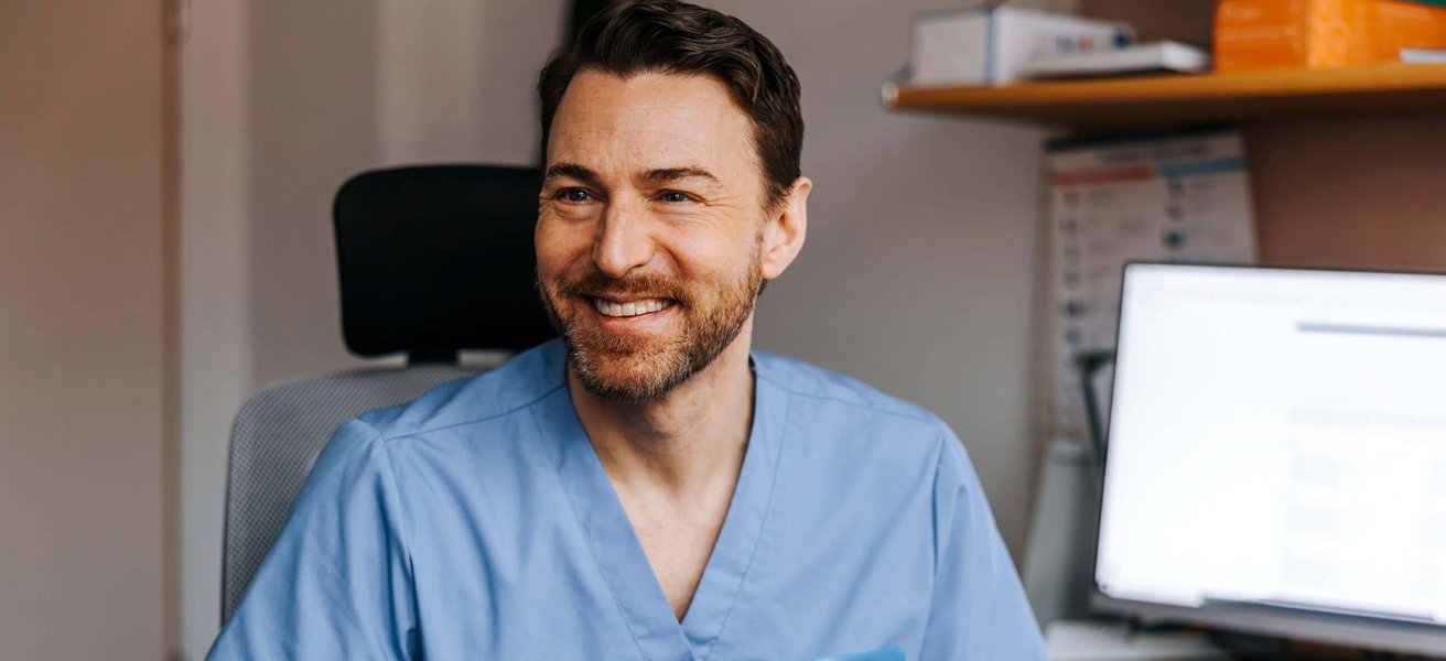 Happy male medical expert holding ear thermometer while talking with patient in examination room