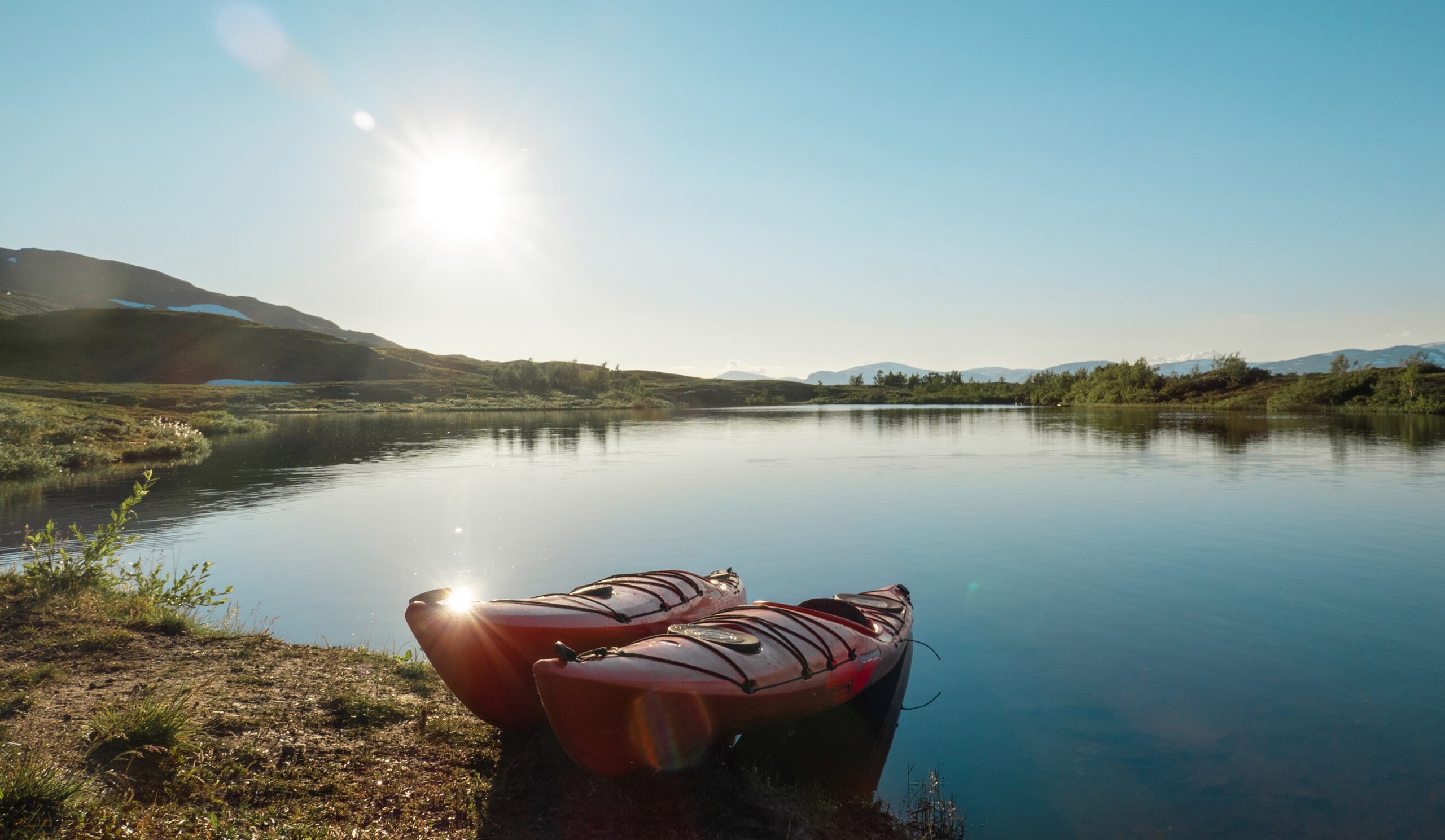 two kayaks pulled up on the shore of a sunny lake