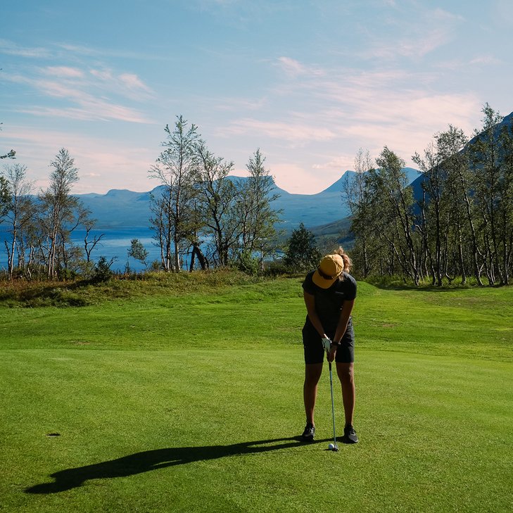 kvinna m&aring;ttar med sin putter p&aring; golfbanan en solig dag med Lapporten i bakgrunden