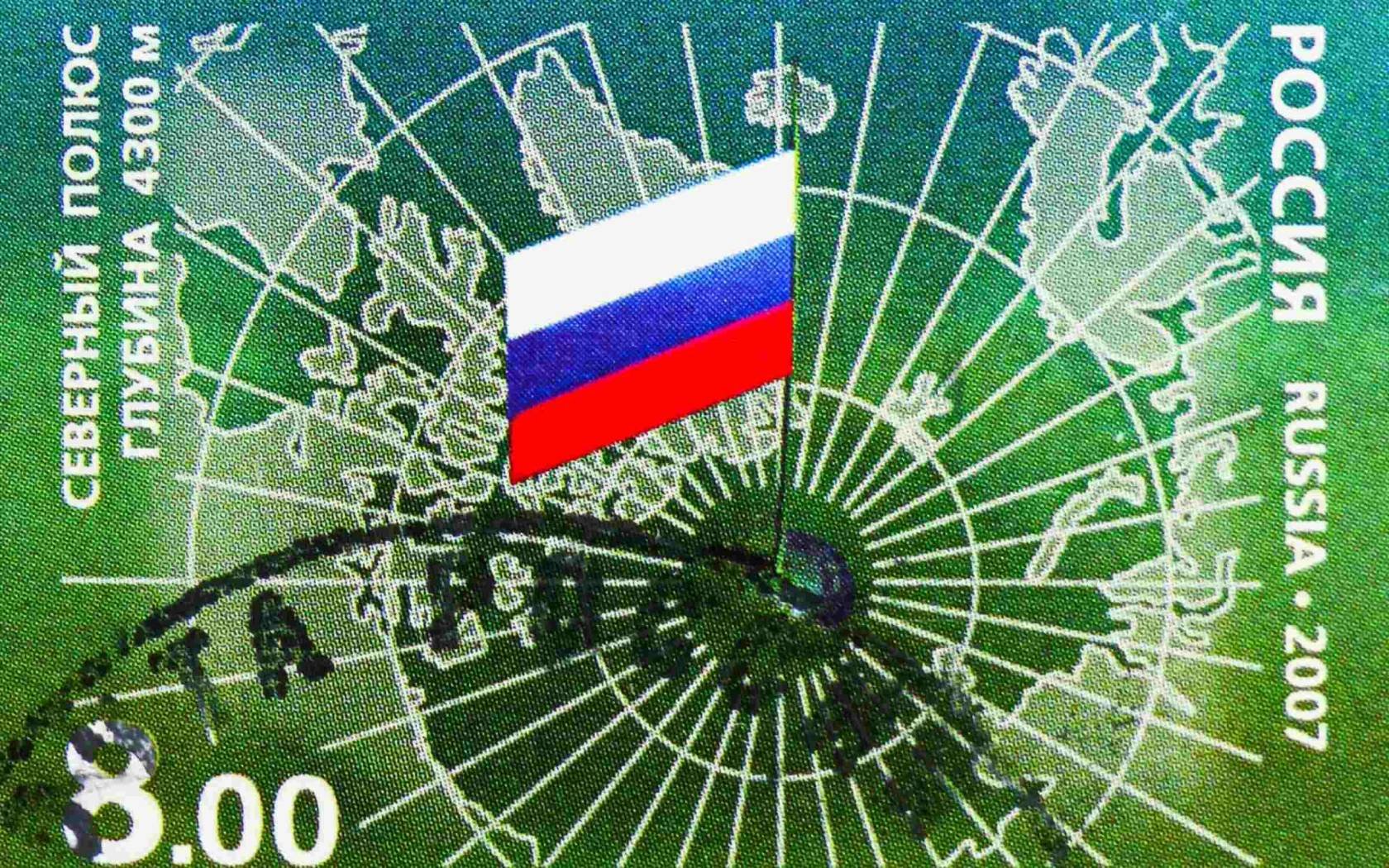 Postage stamp printed in Russia shows a mirrored map of the Arctic, with Russian flag on the North Pole.