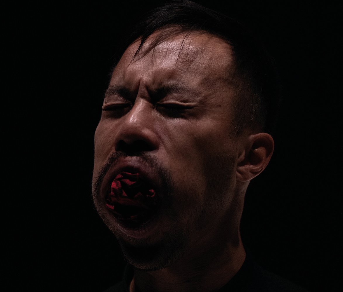 Närbild av en man mot svart bakgrund med slutna ögon och munnen öppen i ett starkt, intensivt uttryck.