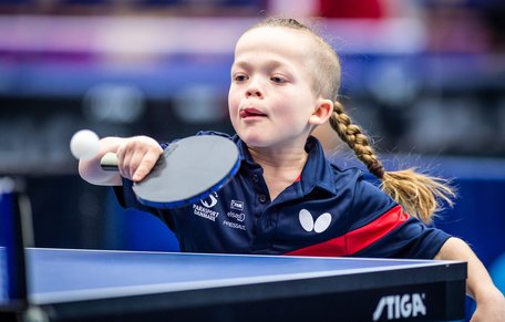 Flicka med lång fläta slår en backhand i bordtennis.