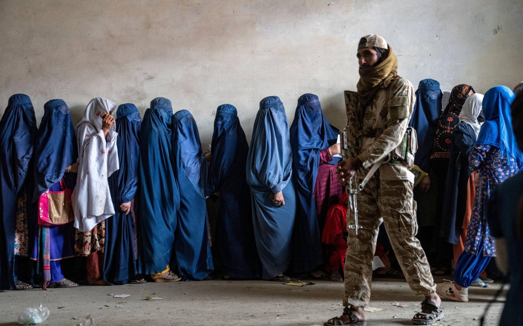 A Taliban fighter stands guard as women wait to receive food rations distributed by a humanitarian aid group in Kabul, Afghanistan, May, 2023.