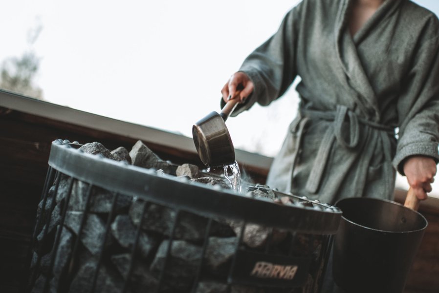 Kvinna med badrock h&auml;ller vatten p&aring; bastuaggregat
