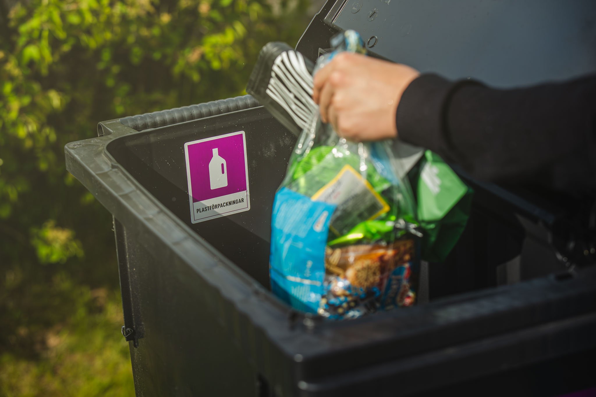 Hand kastar plastflaska i svart sopk&auml;rl m&auml;rkt f&ouml;r plastf&ouml;rpackningar.