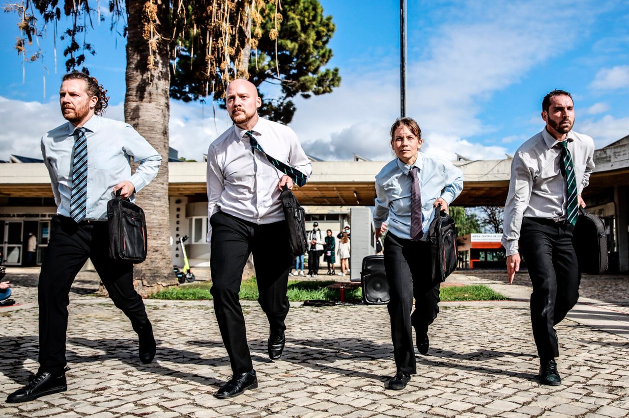 Fyra dansare med kostymbyxor, skjorta och slips med portföljer i händerna.