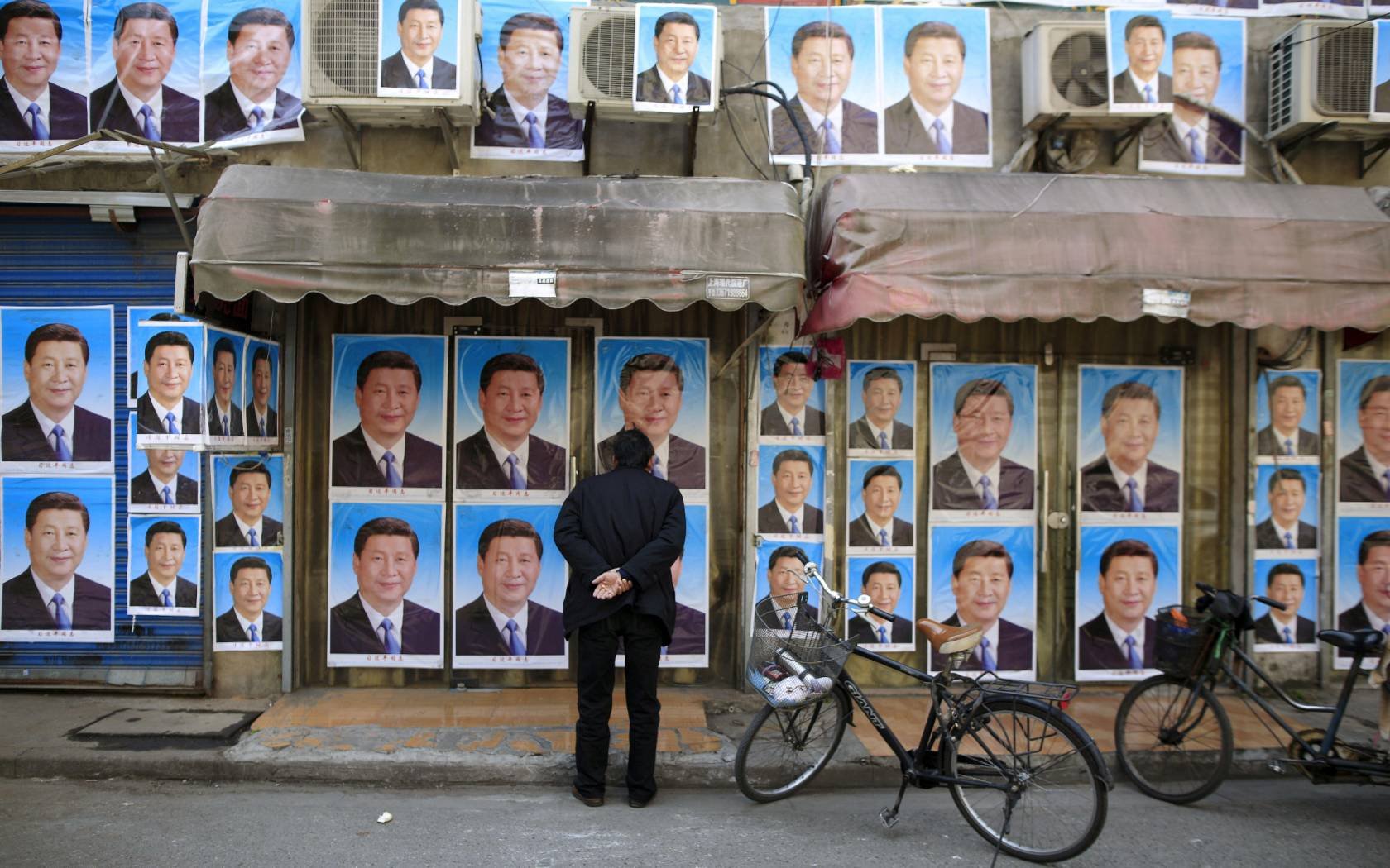 A man looks at a building covered in posters of Chinese President Xi Jinping in Shanghai.