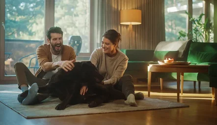 Ett par sitter på golvet i sitt vardagsrum och leker med sin hund.