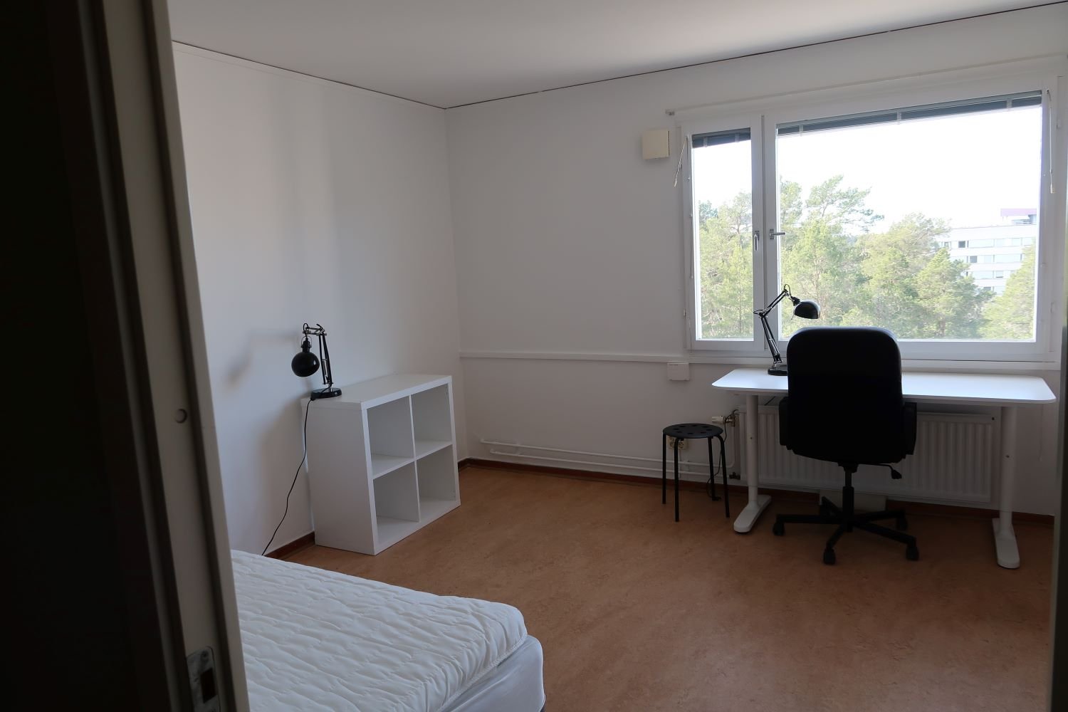 Student room with desk, chair, storage unit, lamp and bed.
