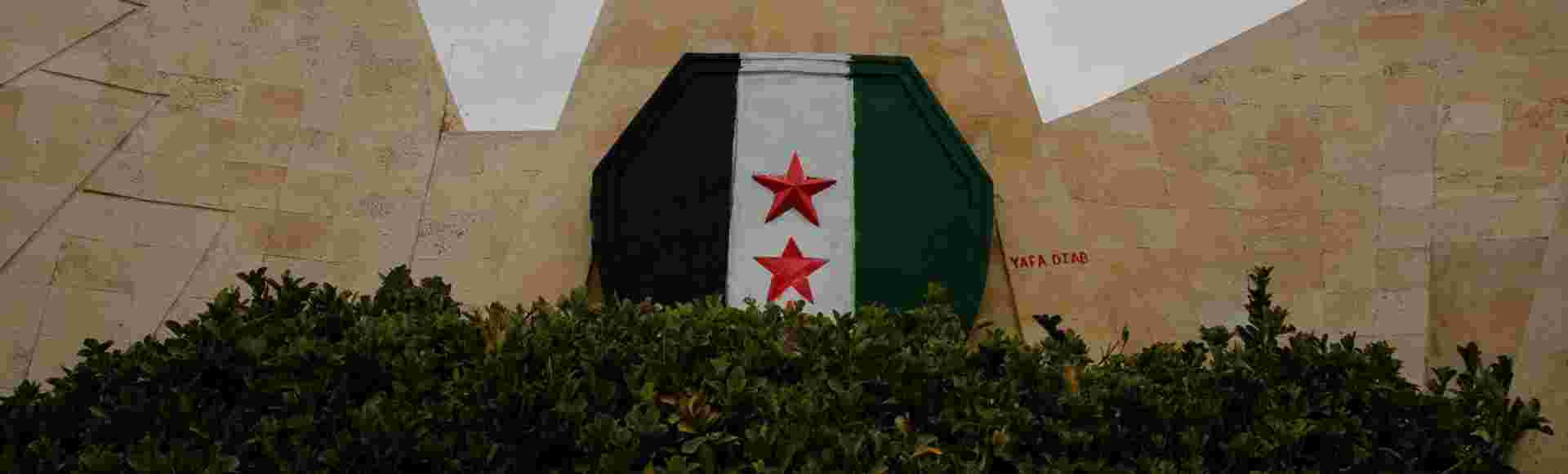 The flag of the Syrian Revolution painted on an eagle-shaped wall in Hama, Syria. 7 December 2024.
