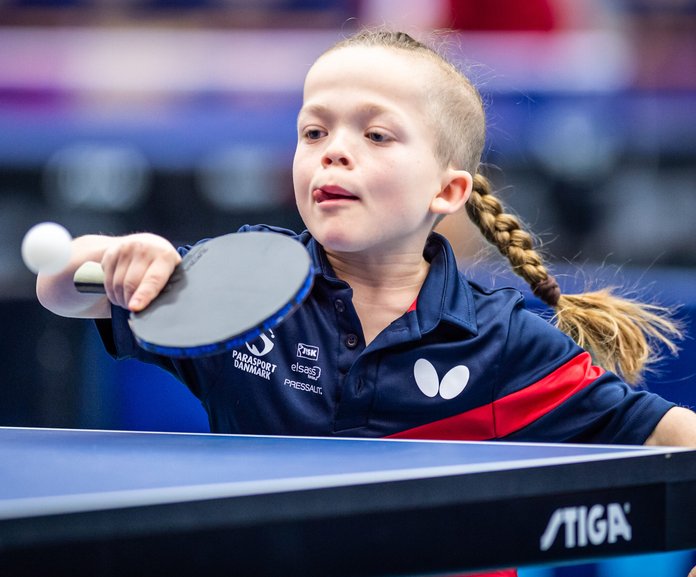 Flicka med lång fläta slår en backhand i bordtennis.