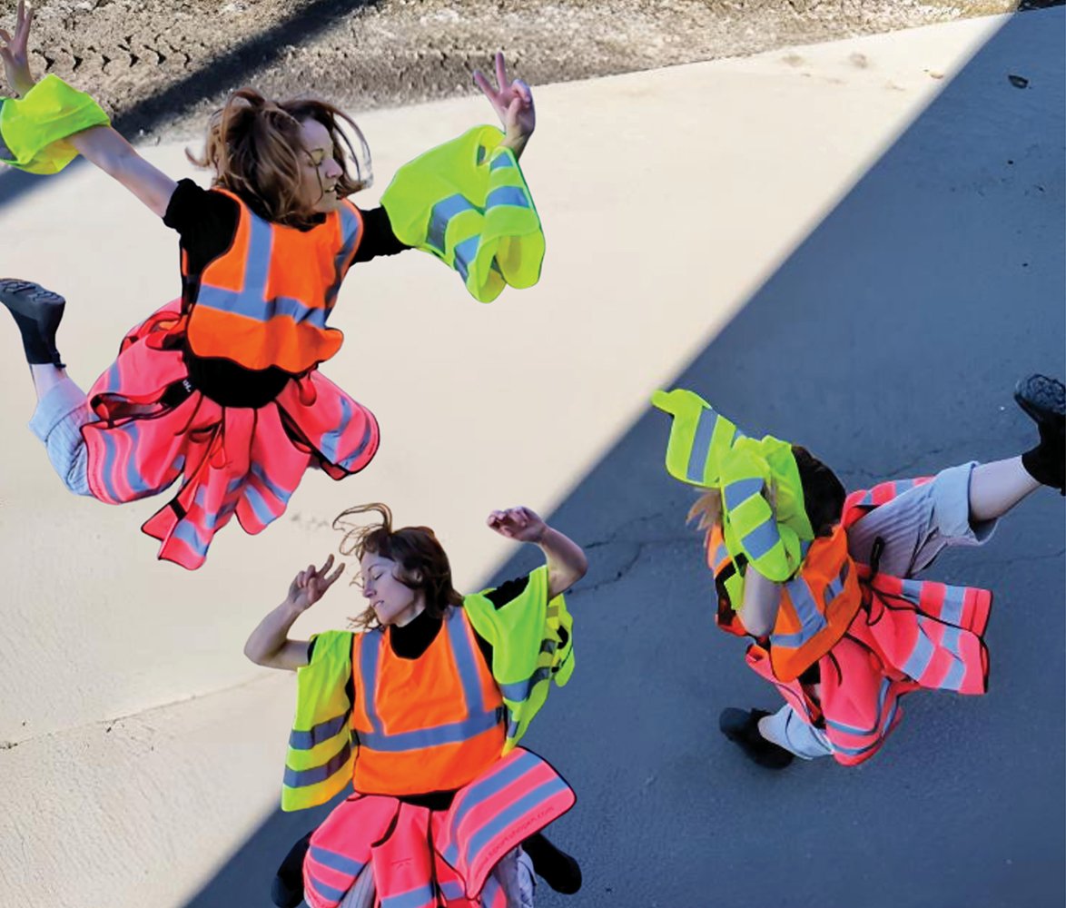 Tre personer i färgglada reflexvästar rör sig dynamiskt ovanifrån sett, som i en koreograferad dans utomhus.