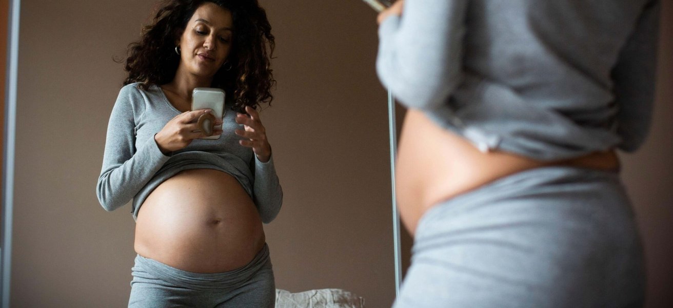 Reflection of pregnant woman taking selfie on smart phone at home