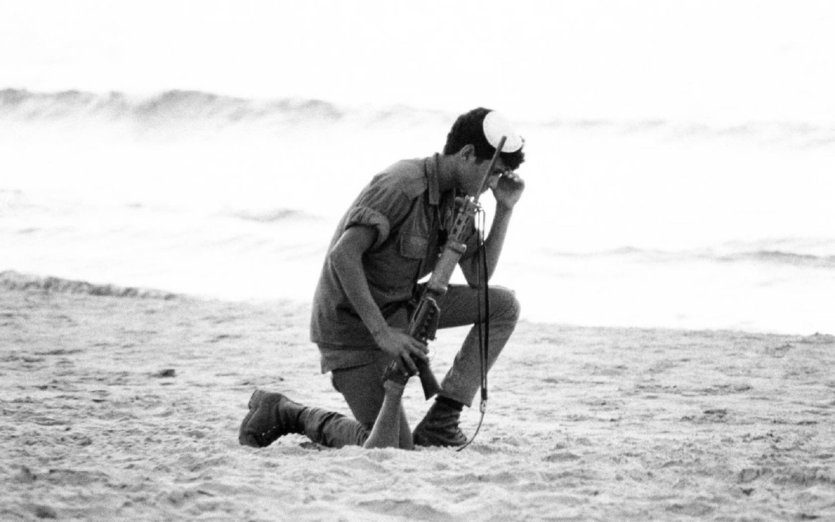 Israeli soldier kneels down to pray in the sand during the Yom Kippur War.