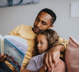 Father reading book with daughter while sitting at home
