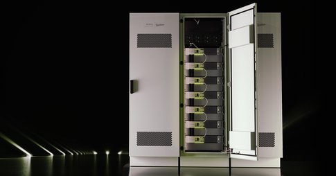 Lithium-ion batteries are shown against a black background, slightly lit up by lights on the floor on the left side.