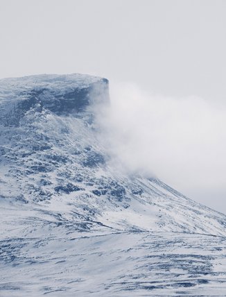 en sn&ouml;bekl&auml;dd fj&auml;lltopp omgiven av moln