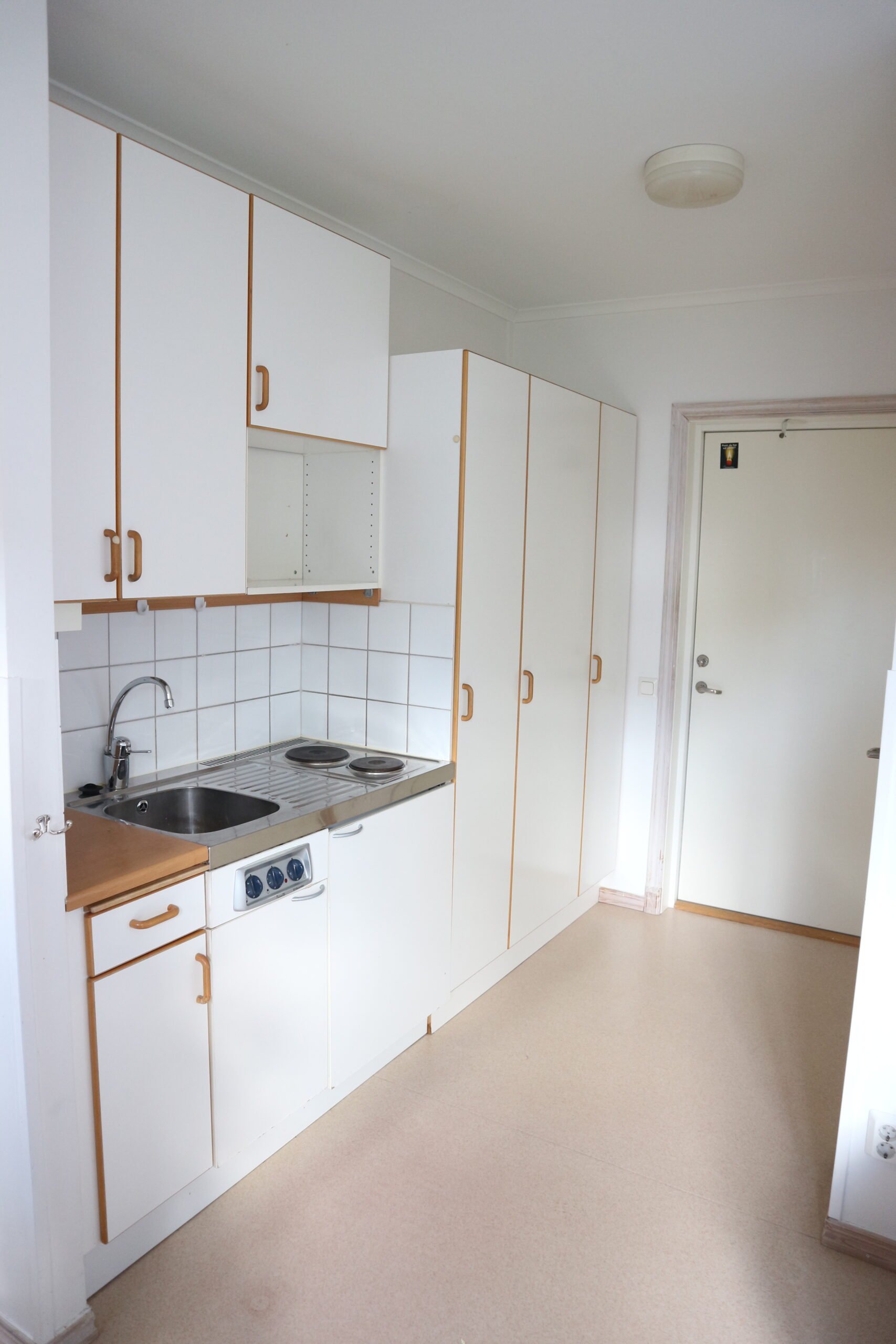 Student room with kitchenette: sink, cupboards, stove top and small refrigerator.