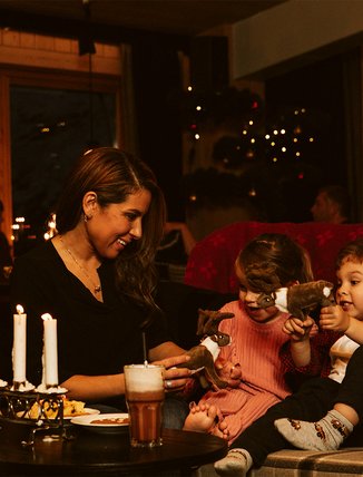 A mother is playing with her two children next to an Advent candleholder